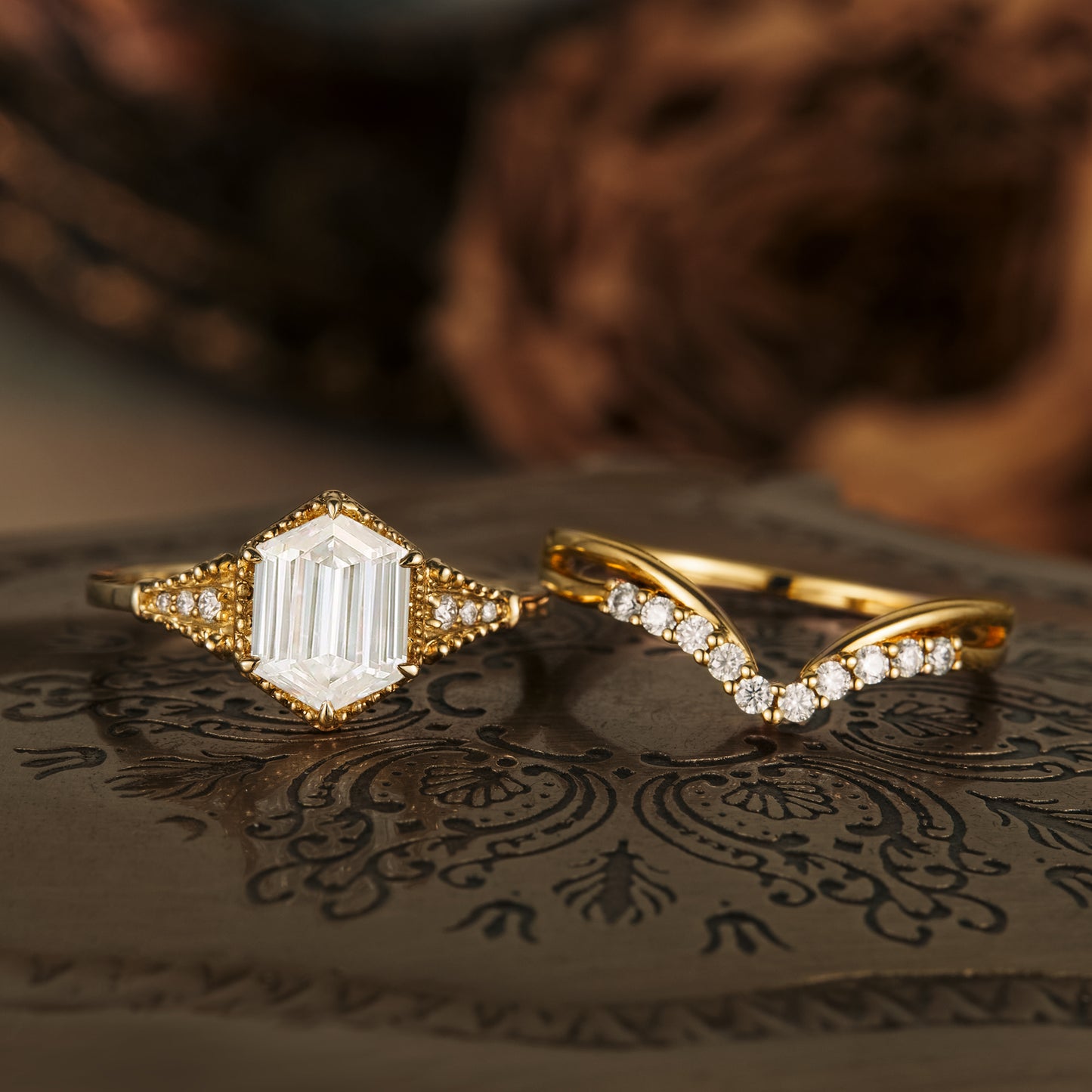 Elegant long-hexagon Moissanite ring set with gold bands on decorative surface