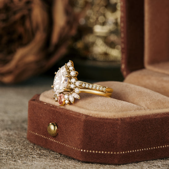 Elegant golden pear Moissanite engagement ring set with floral wedding band on velvet.