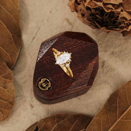 Nature-inspired marquise moissanite ring on wooden box with leaves.