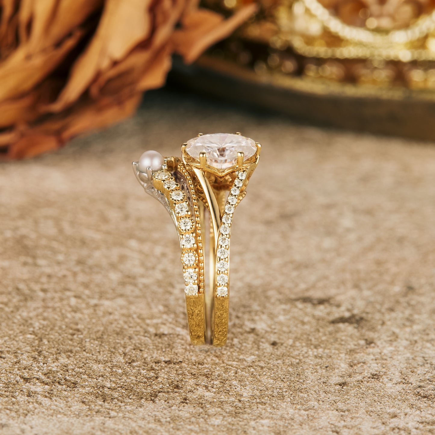 Moissanite and pearl ring set on a textured surface with golden accents.