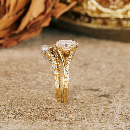 Moissanite and pearl ring set on a textured surface with golden accents.