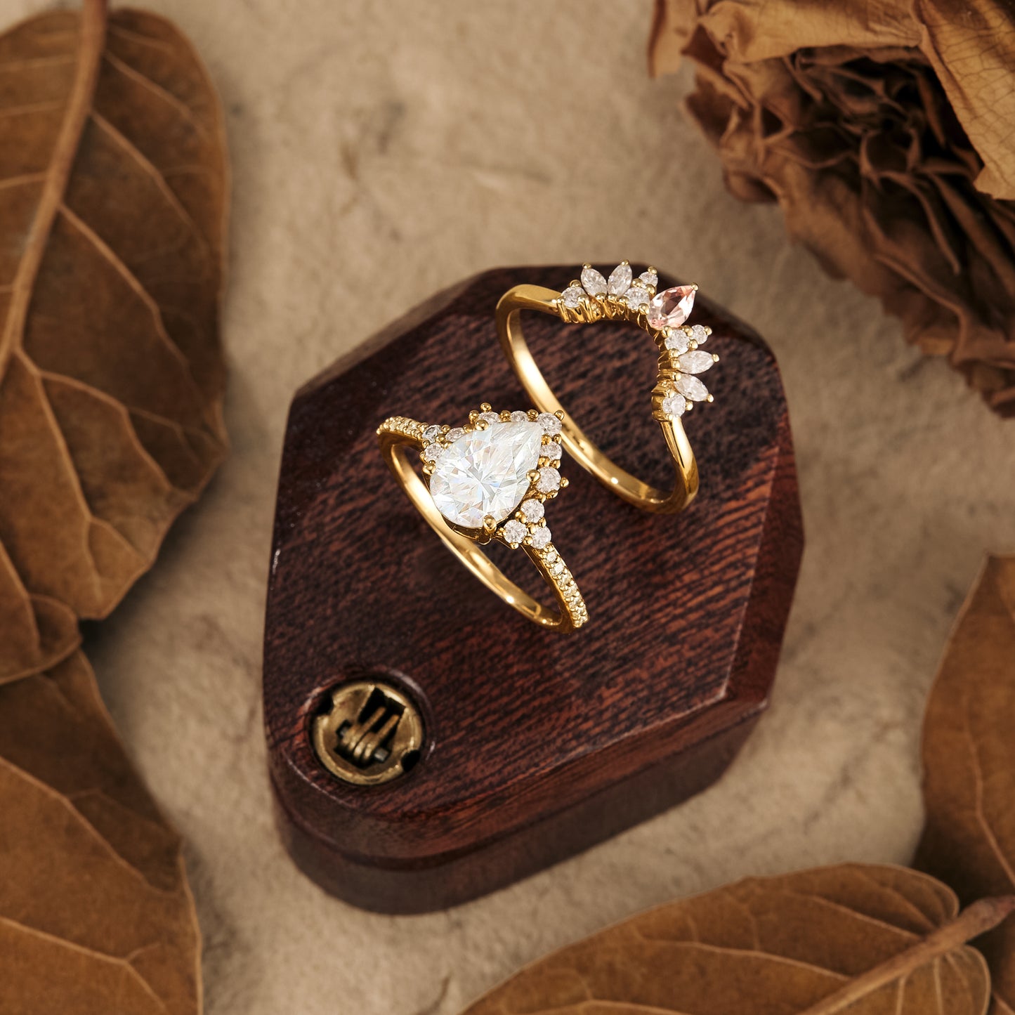 Gold pear Moissanite halo engagement ring with floral wedding band on wooden display.