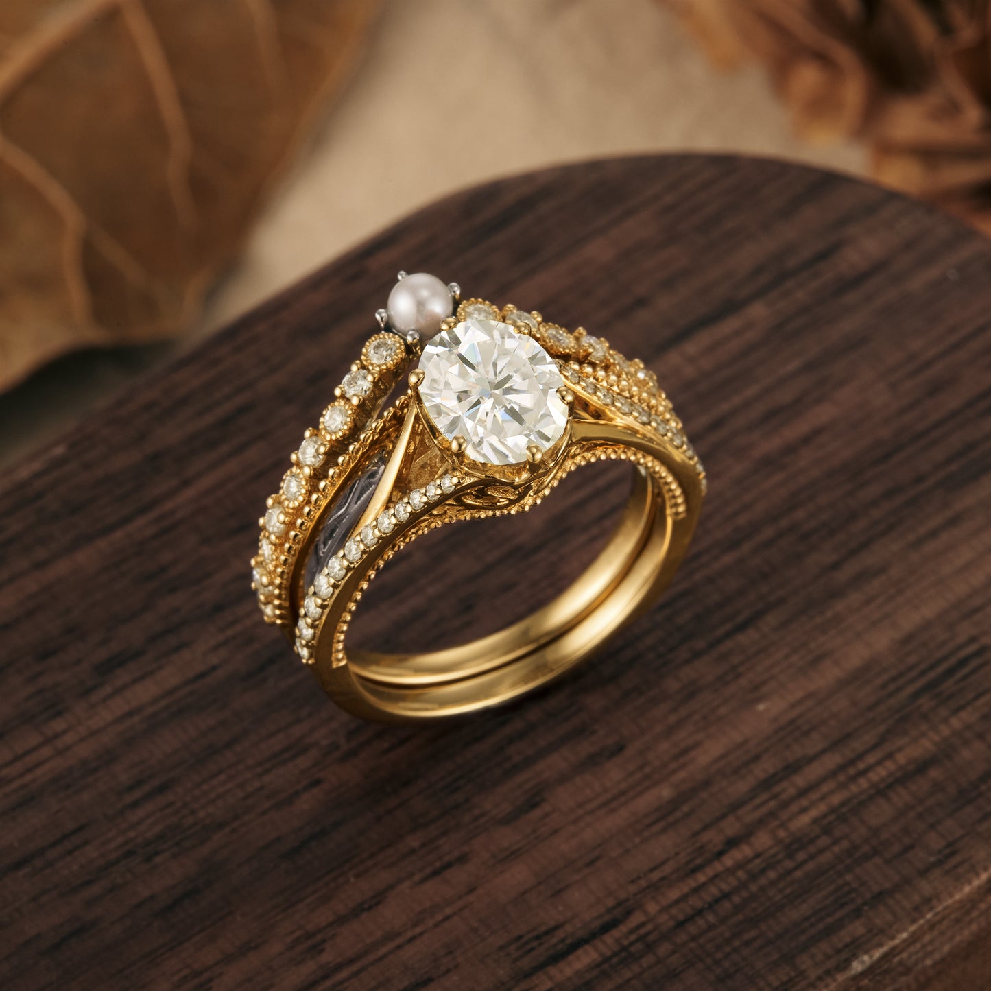 Moissanite and pearl engagement ring set with intricate gold band on wooden surface