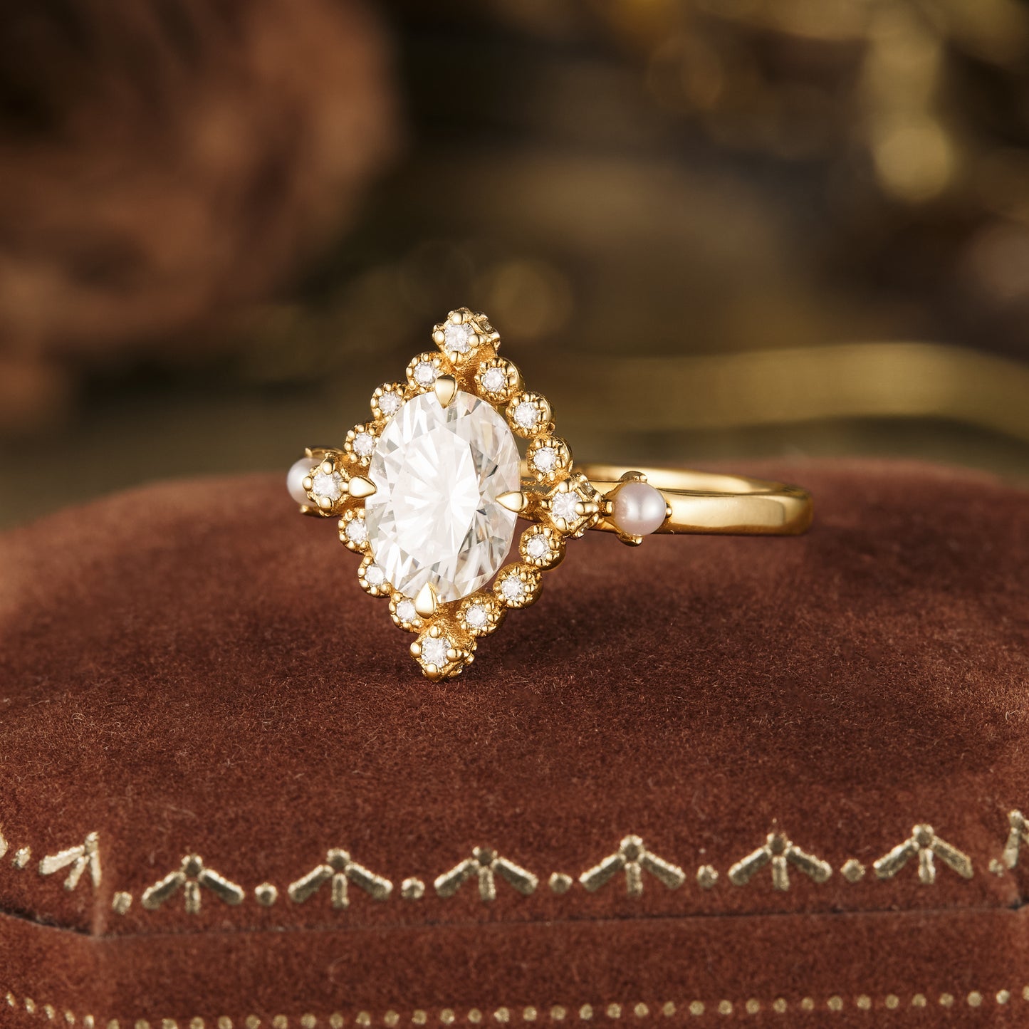 Gold ring with oval moissanite and pearl accents on velvet ring box.