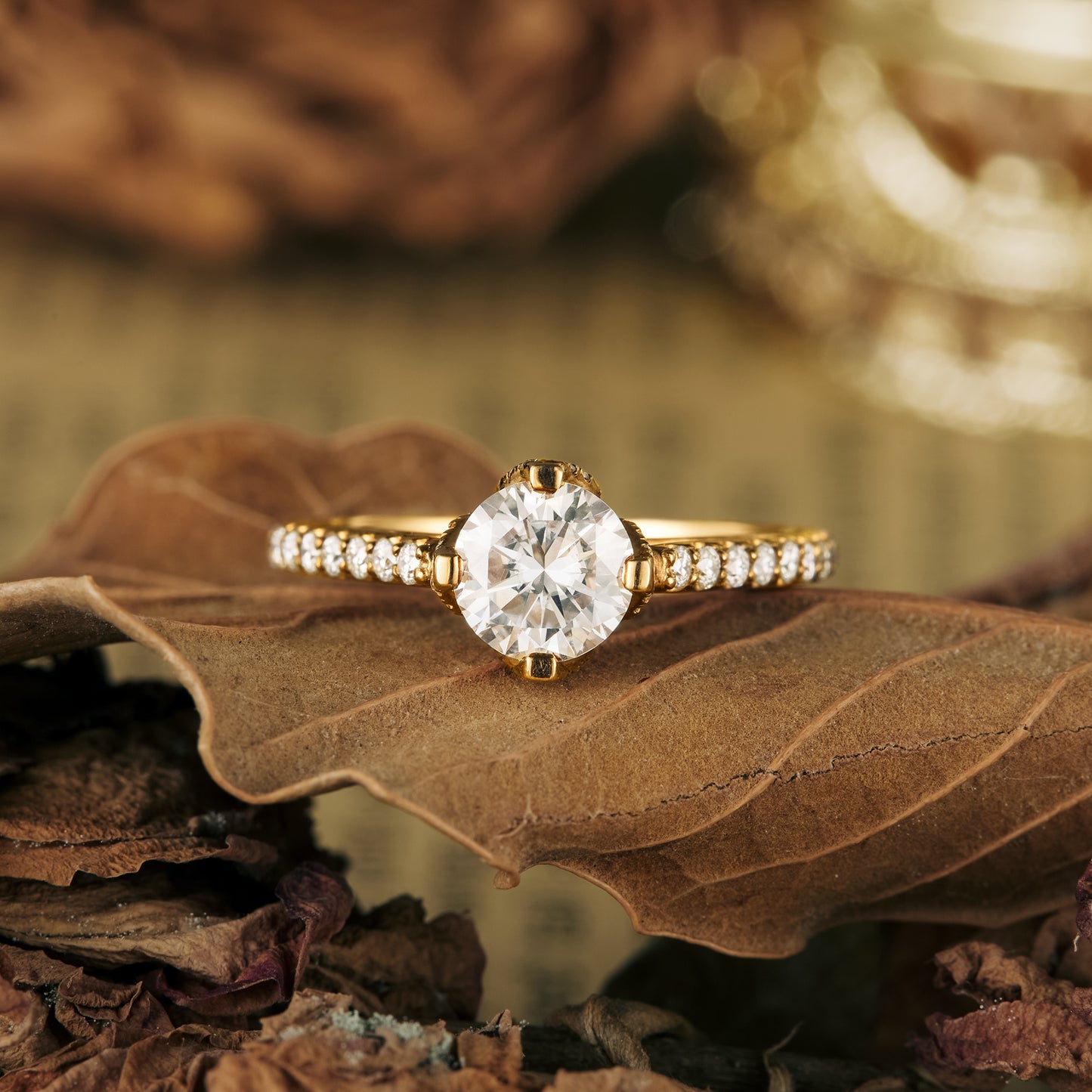 Moissanite engagement ring with round center stone and gold band on dried leaves