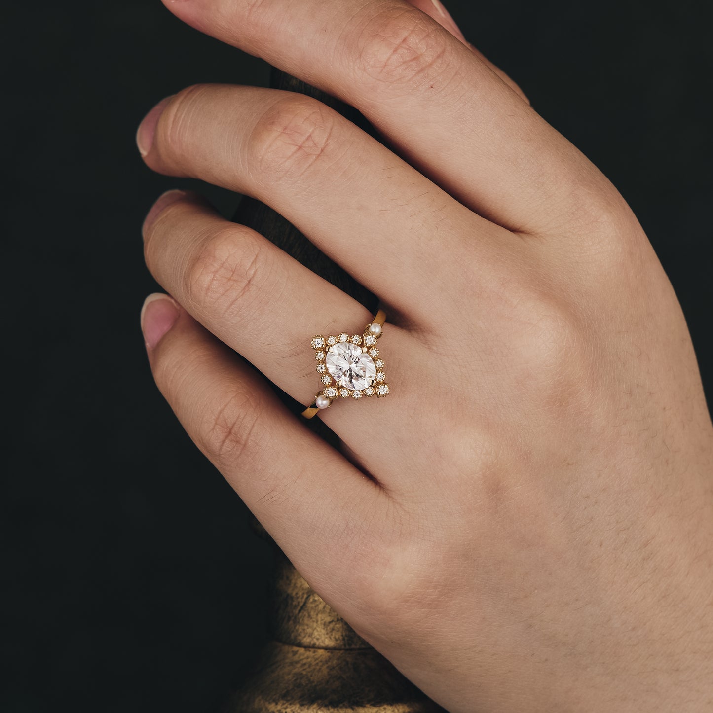 Moissanite ring with oval stone and diamond halo on hand, showcasing elegant design.
