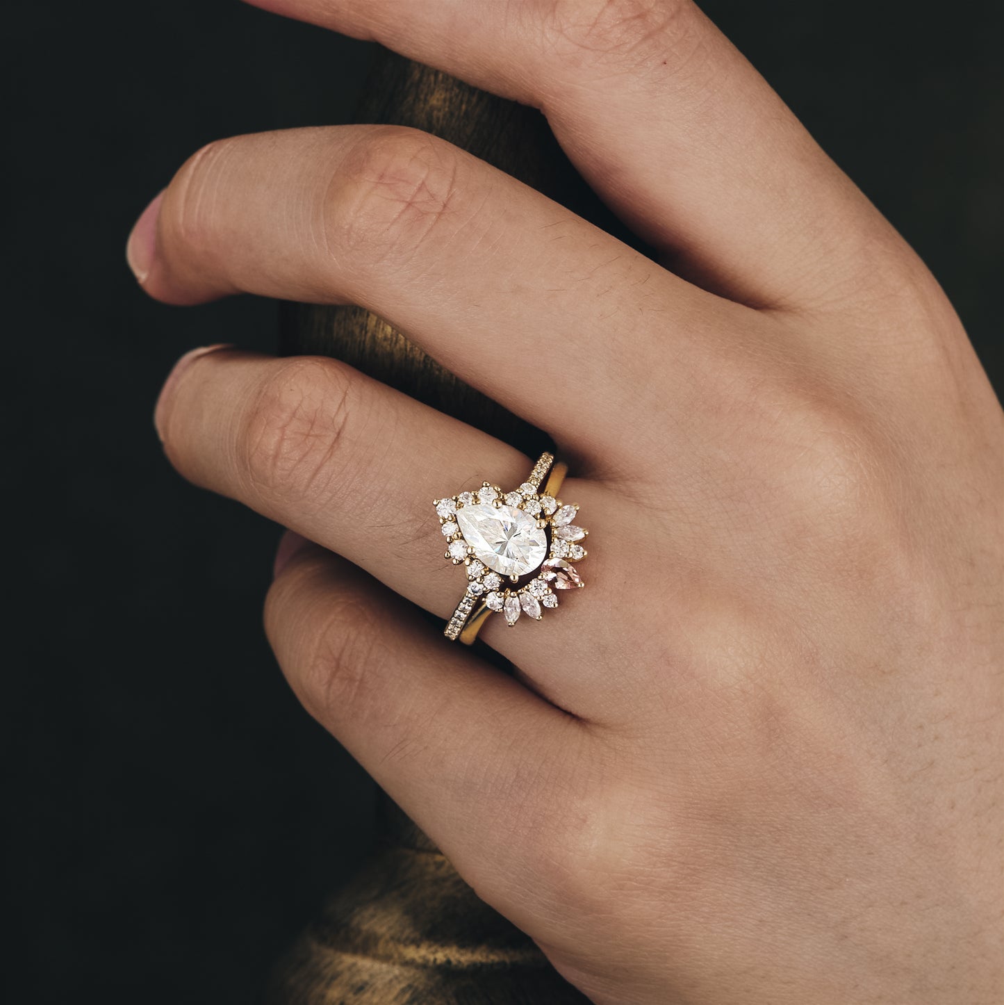 Moissanite pear engagement ring with floral halo and matching wedding band on hand