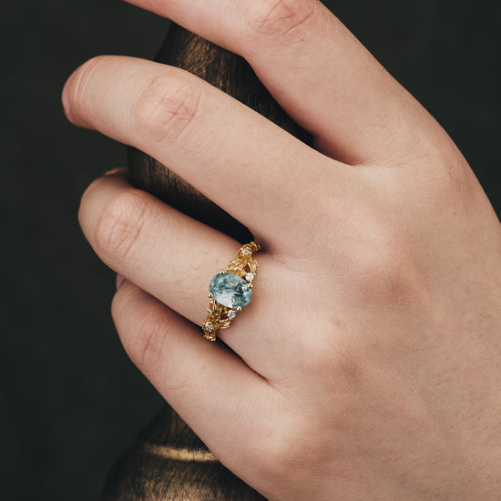 Aquamarine engagement ring on a hand, featuring a leaf-themed gold band.