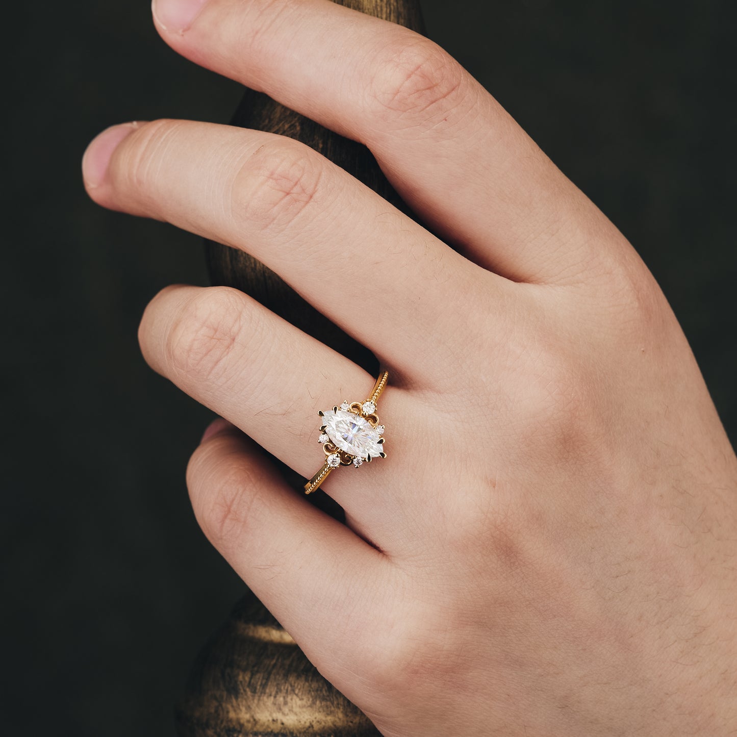 Hand wearing marquise moissanite ring with gold band and delicate details