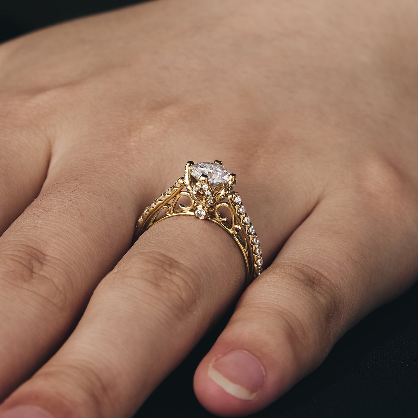 Dazzling moissanite engagement ring on hand with intricate gold detail and round center stone.