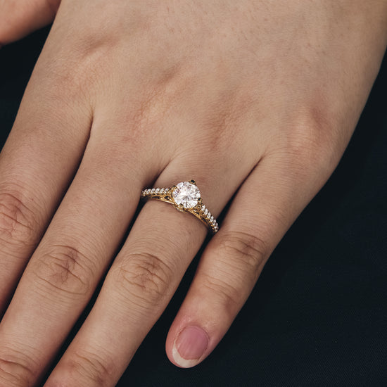 Moissanite engagement ring with round center stone and detailed gold band on hand.