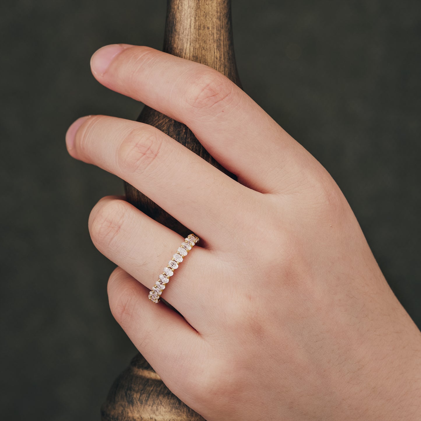 Hand wearing gold moissanite oval eternity wedding band with sparkling stones.