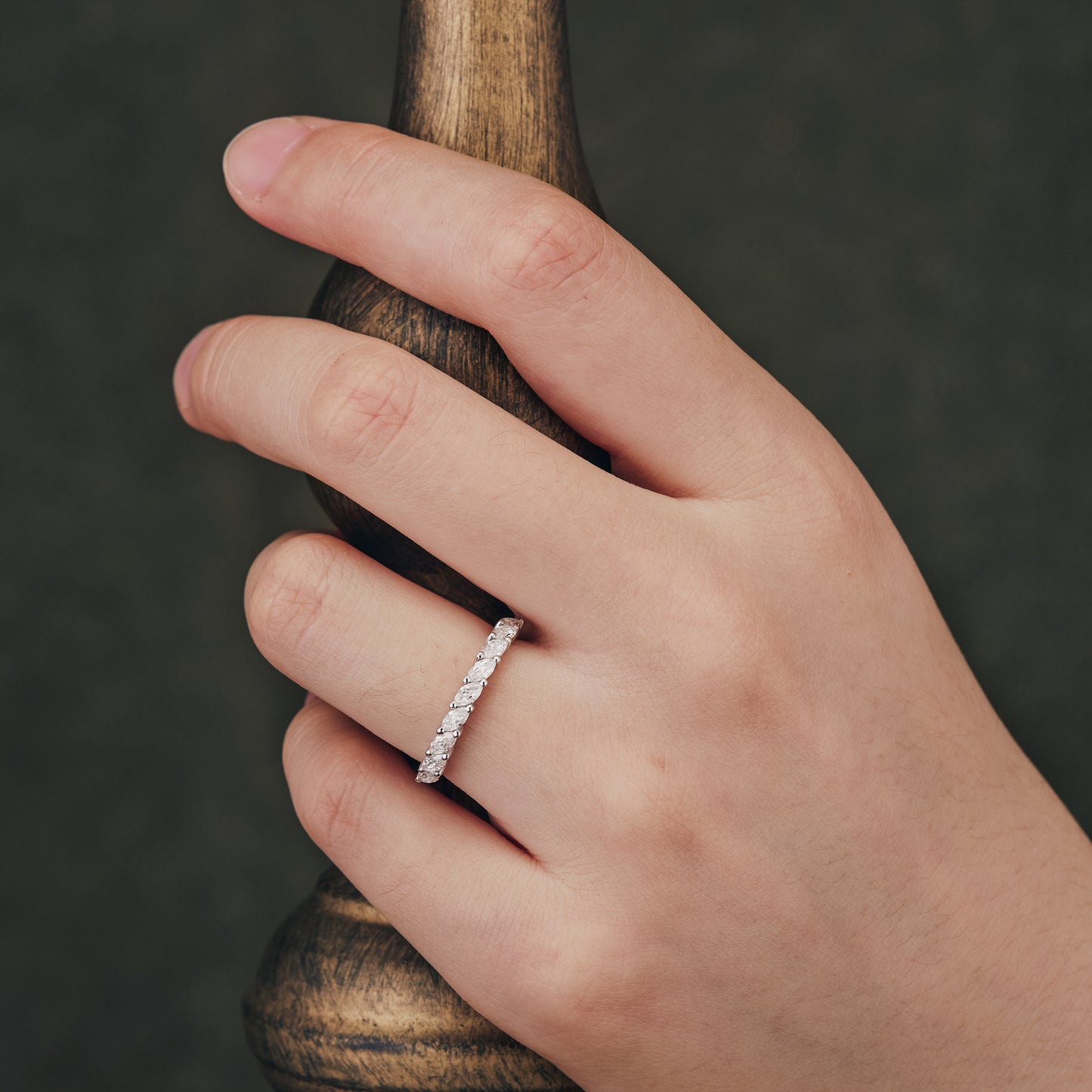 Hand showcasing marquise-cut moissanite wedding band against a wooden backdrop
