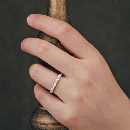 Hand showcasing marquise-cut moissanite wedding band against a wooden backdrop