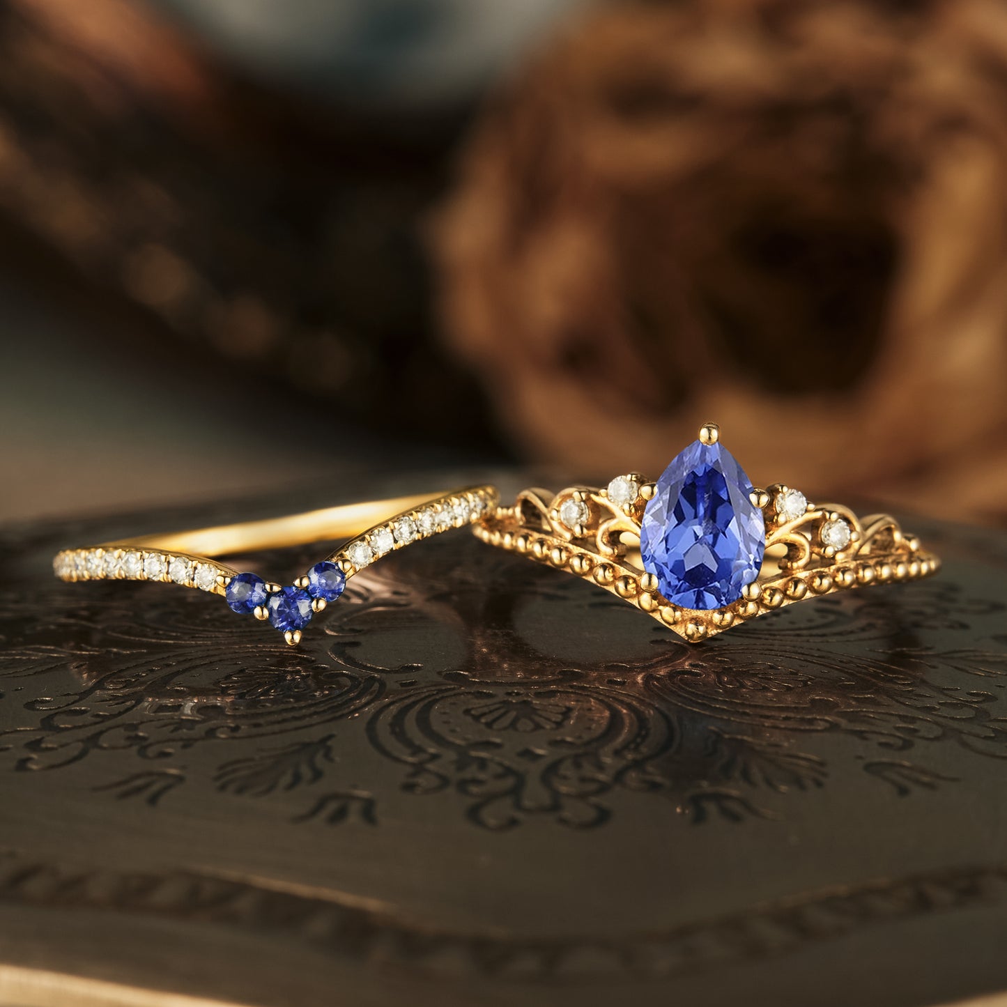 Gold engagement ring set with pear-shaped sapphire and accent diamonds, intricate design.