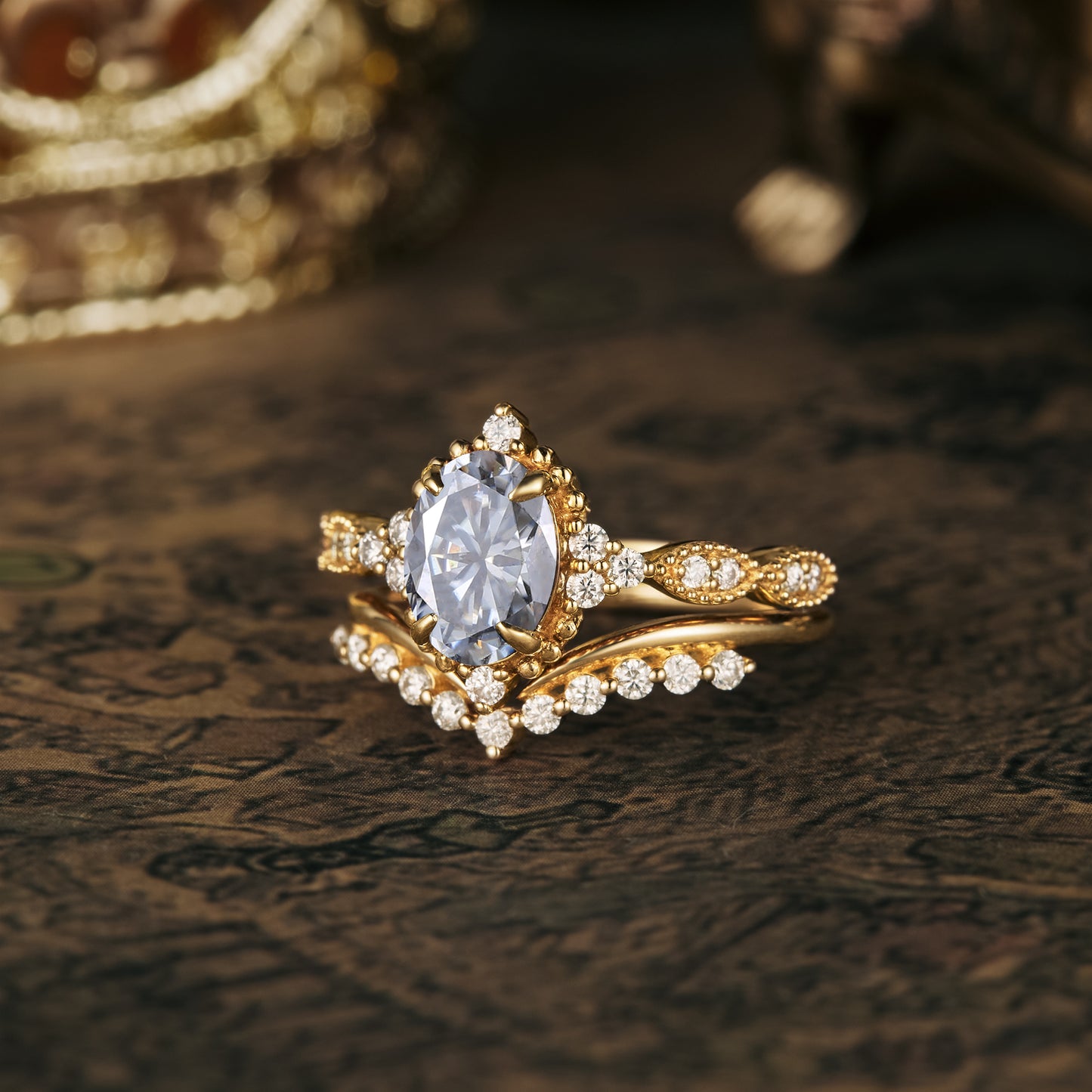 Gold ring set with oval gray moissanite and round accents on ornate background.
