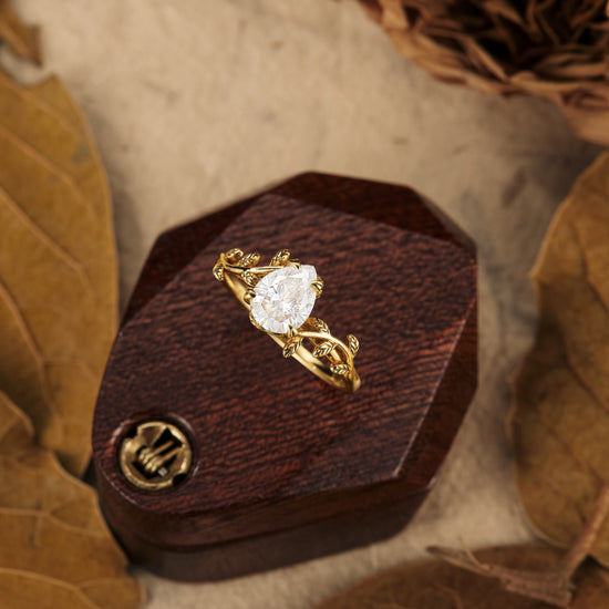 Pear-shaped moissanite ring with intricate gold leaf details on a wooden display.