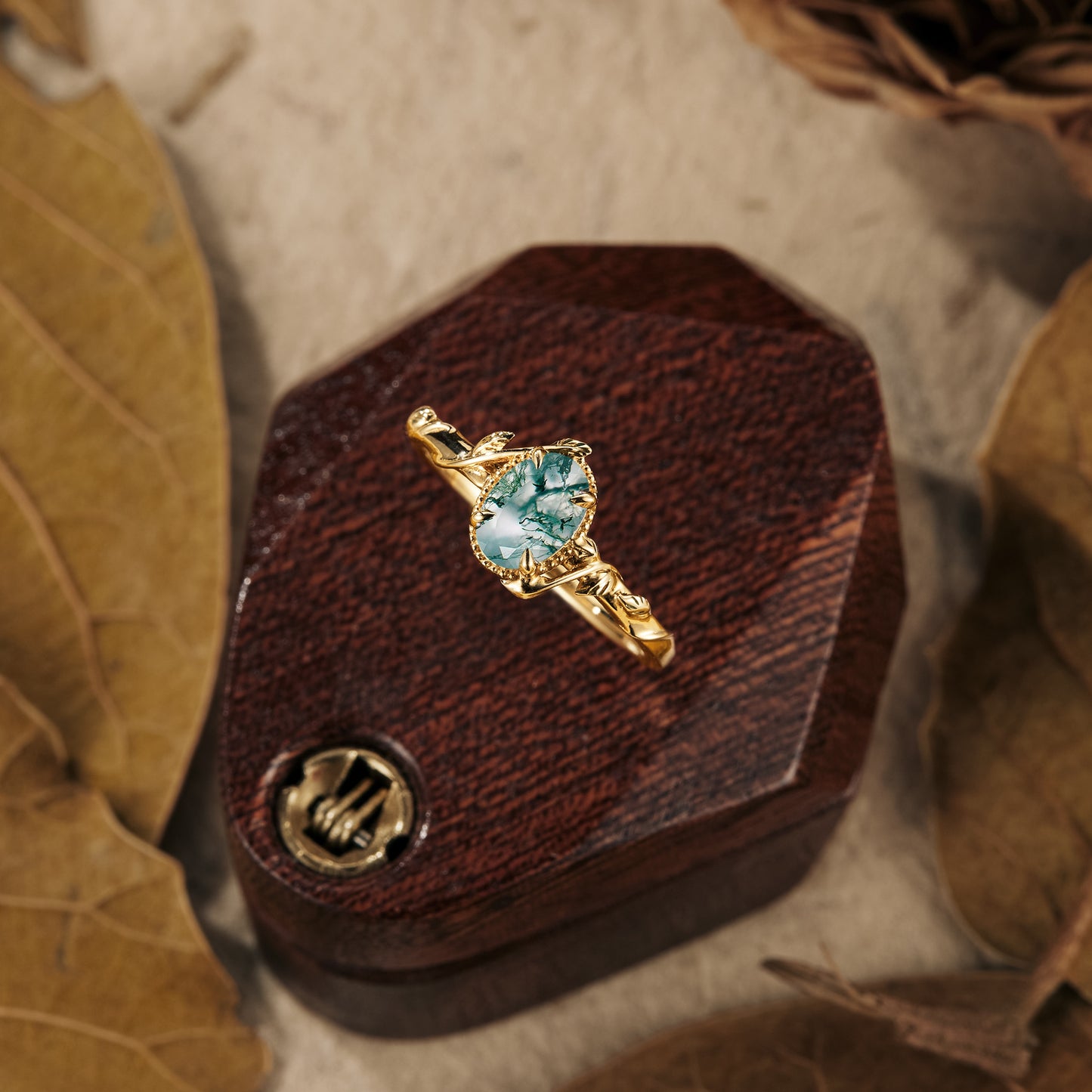 Moss agate oval engagement ring with elegant gold leaf accents on wooden display.