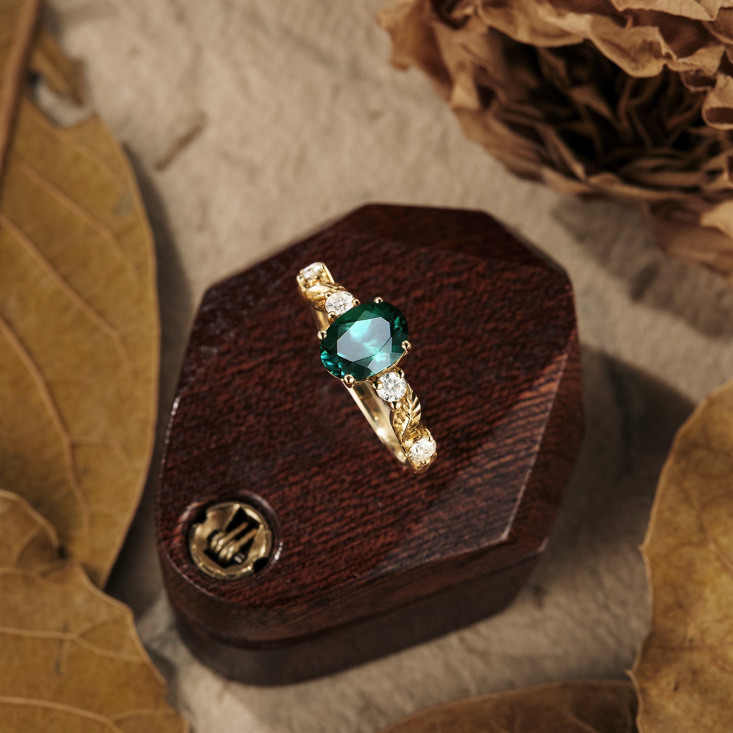 Unique emerald leaf engagement ring on rustic wooden box, featuring moissanite accents