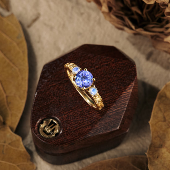 Tanzanite engagement ring with moonstone accents on a wooden box, nature-inspired design.