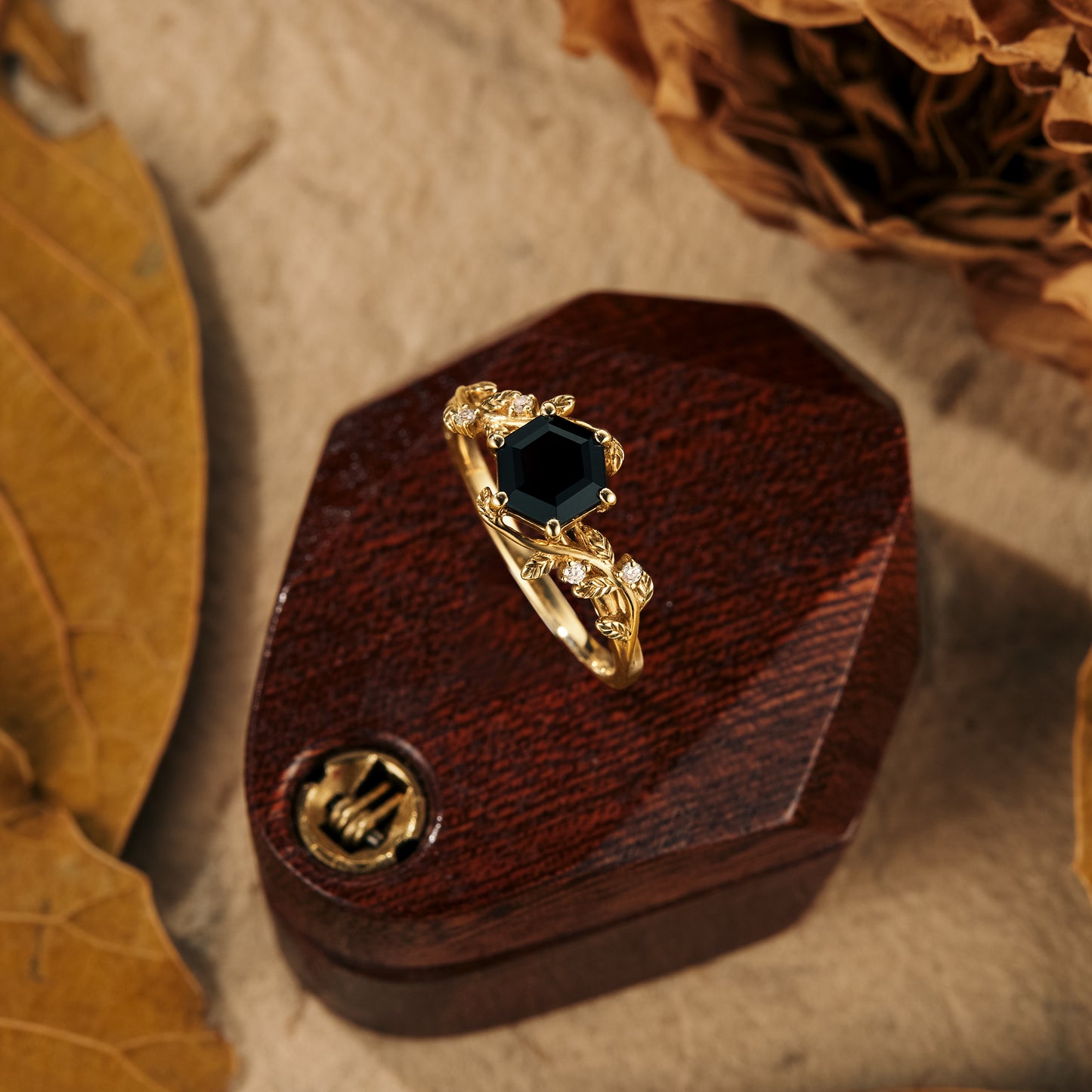 Black onyx hexagon engagement ring with leaf accents and moissanite, on a wooden display.