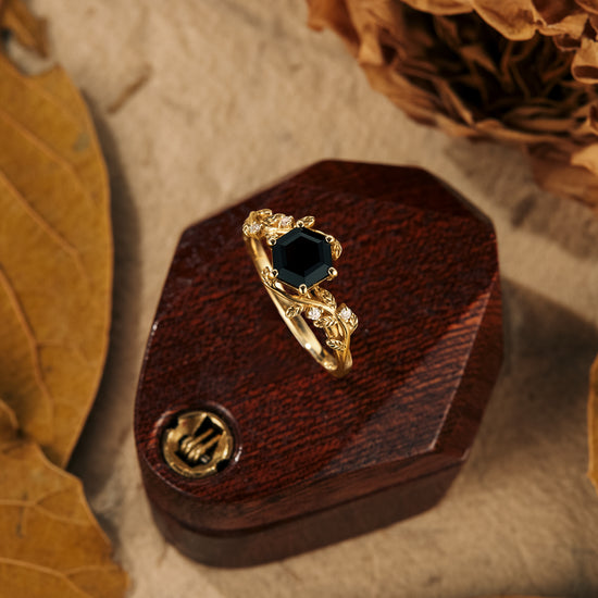 Black onyx hexagon engagement ring with leaf accents and moissanite, on a wooden display.