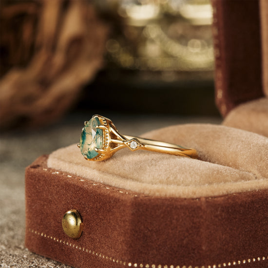 Pear-shaped moss agate ring with gold band and moissanite stone in velvet jewelry box