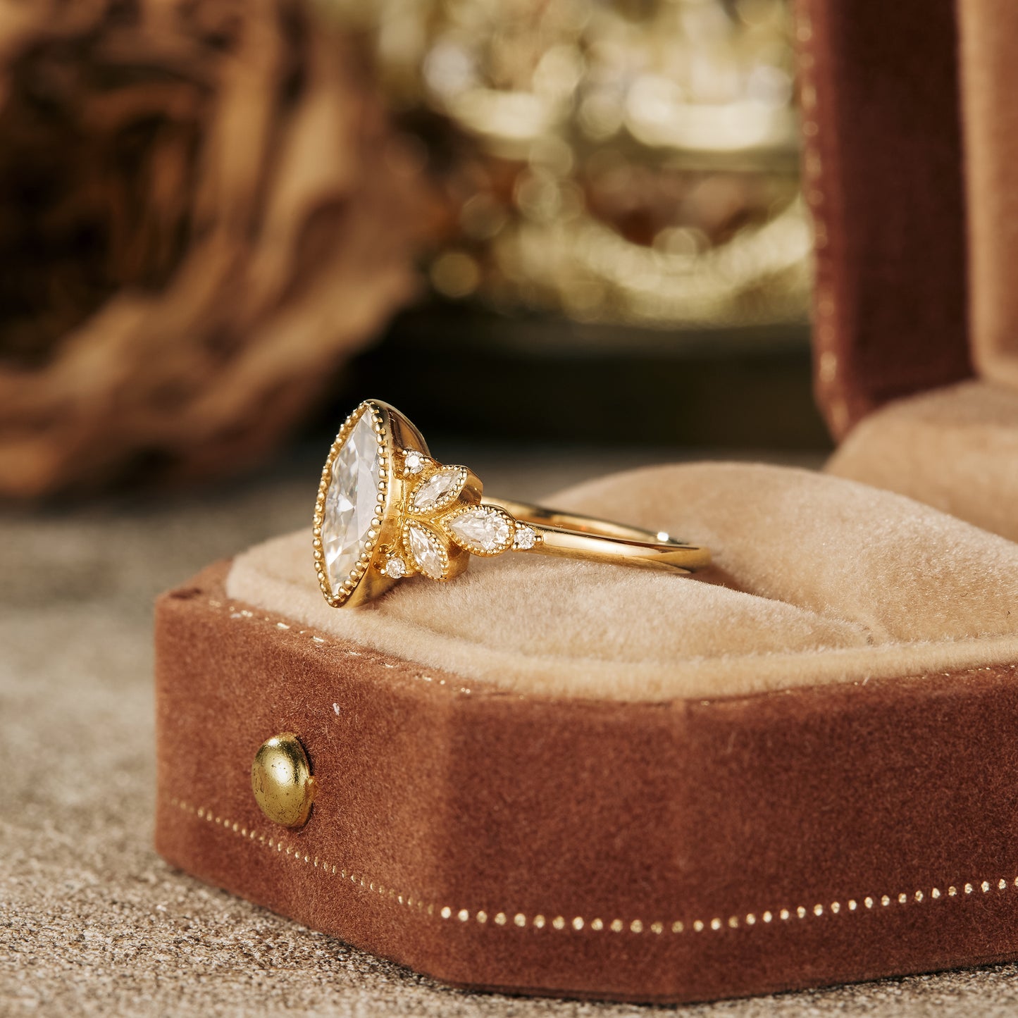 Marquise moissanite engagement ring in gold with floral details on plush ring box.