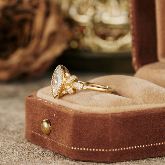 Marquise moissanite engagement ring in gold with floral details on plush ring box.