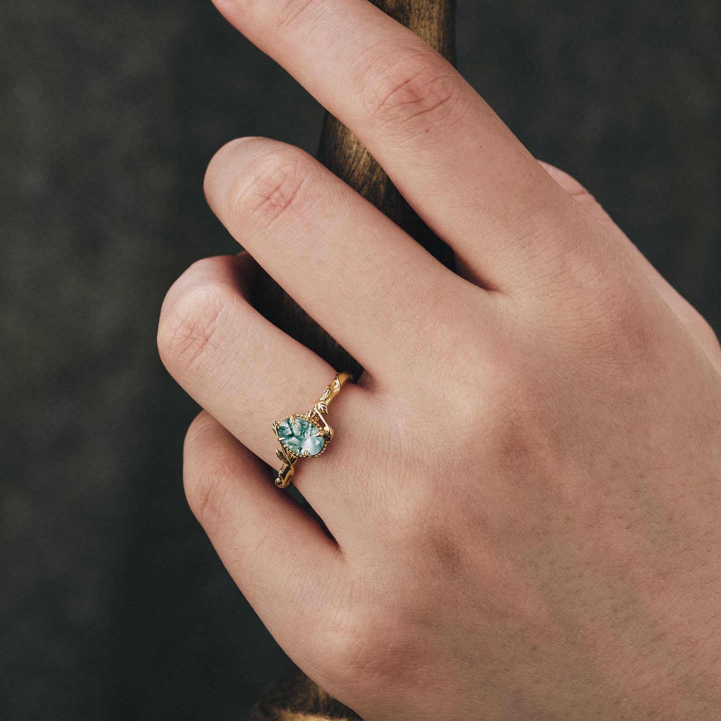Hand wearing moss agate leaf engagement ring with twisted gold band.
