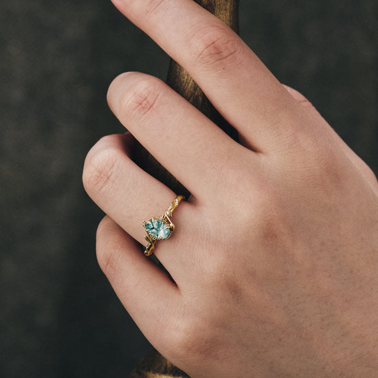 Hand wearing moss agate leaf engagement ring with twisted gold band.