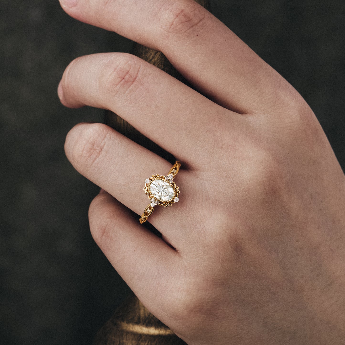 Ornate gold engagement ring featuring oval moissanite on a hand.