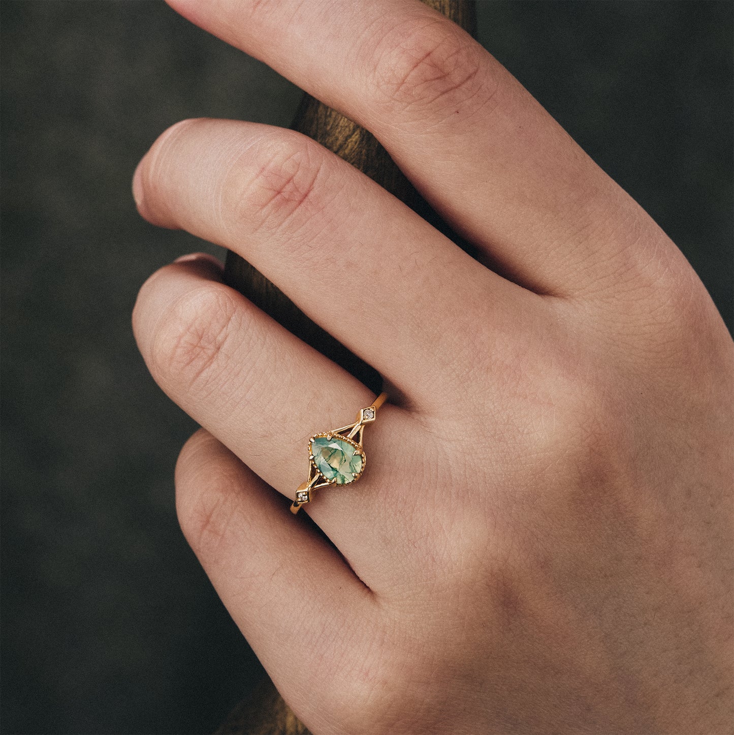 Elegant moss agate pear ring worn on hand with gold band and moissanite accents