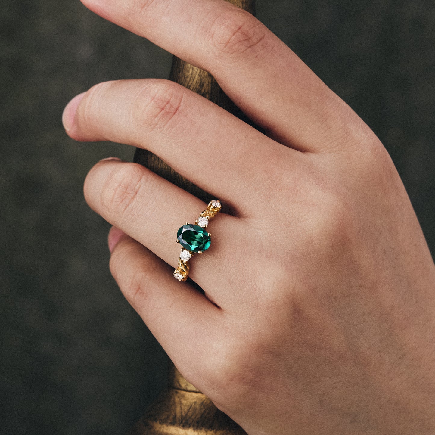 Elegant oval emerald engagement ring on hand with moissanite accents