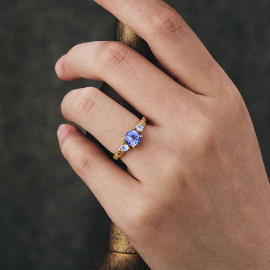 Round tanzanite engagement ring with moonstone accents on a hand